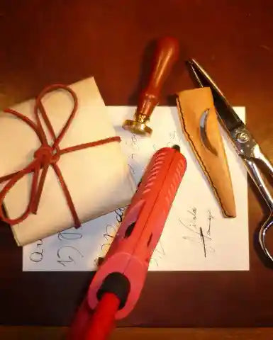 Hot glue gun, wrapped gift, scissors, and sealing wax on a wooden surface